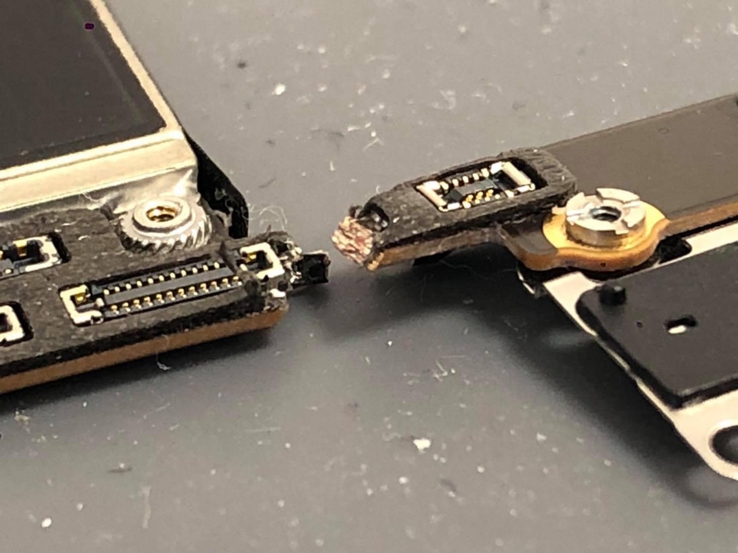 Uszkodzone złącze taśmy flex w smartfonie, widoczne oderwane styki i ślady korozji na płytce drukowanej.