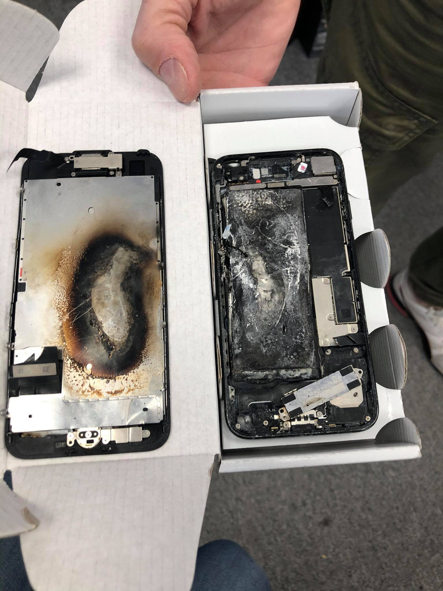 Dwa uszkodzone telefony w otwartym pudełku, widoczne ślady spalenizny i uszkodzenia wewnętrznych komponentów.