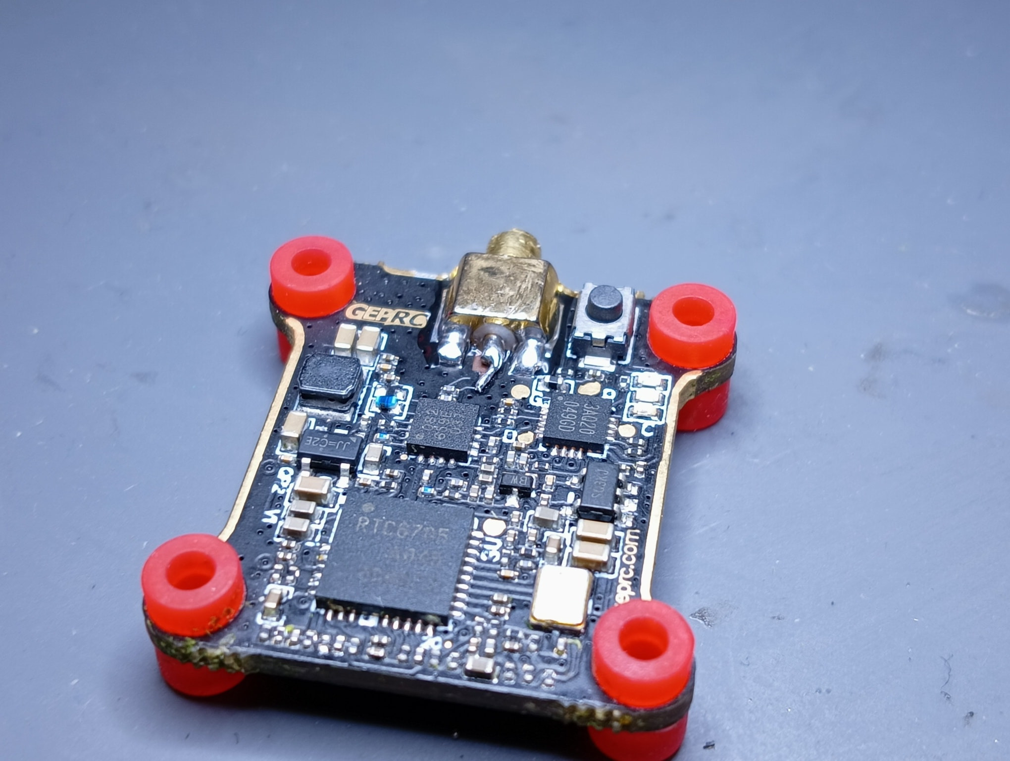 Zdjęcie płytki kontrolera lotu drona z widocznymi elementami elektronicznymi i anteną, wykonane w Poznaniu. Czarna płytka z czerwonymi amortyzatorami. Widoczne ślady lutowania i oznaczenia...