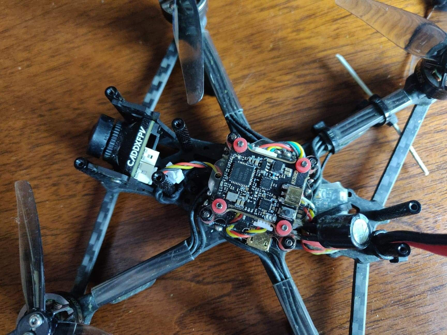 Wnętrze drona FPV z widoczną płytą główną, kamerą Caddx FPV i elementami konstrukcyjnymi na drewnianym tle.