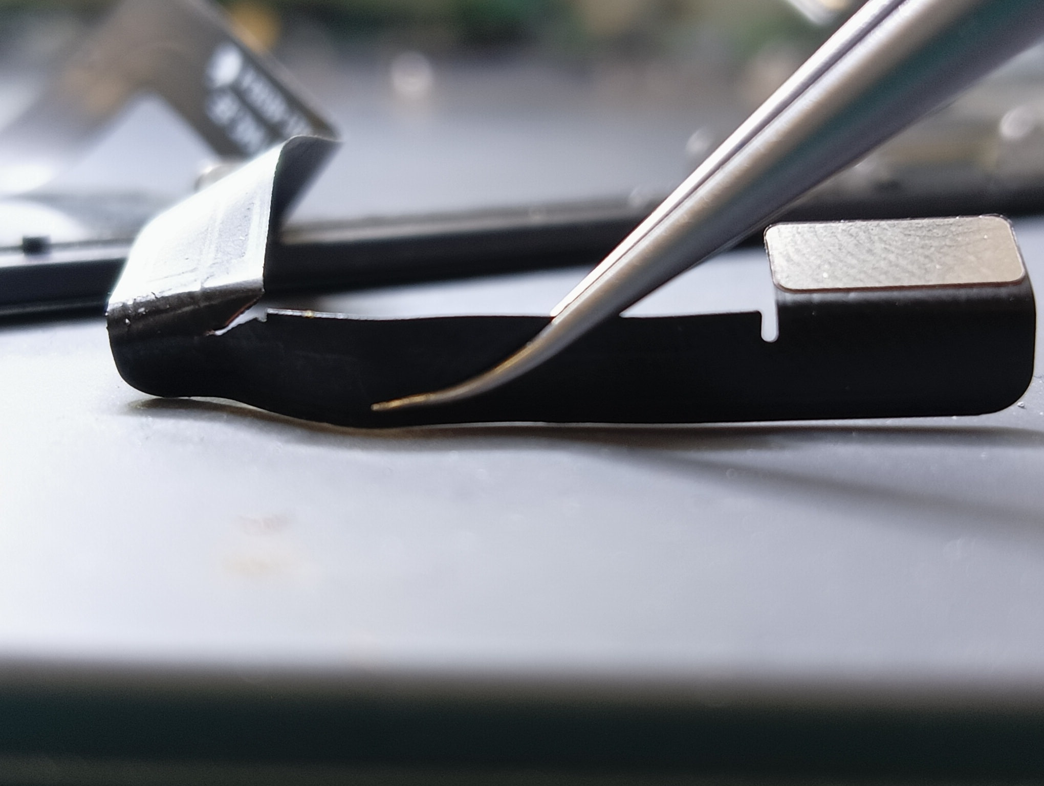 Precyzyjne użycie pęsety do manipulowania delikatnym elementem elektroniki, prawdopodobnie podczas wymiany lub naprawy podzespołu w urządzeniu komputerowym.