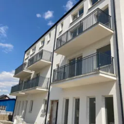 Nowo wybudowany budynek mieszkalny z balkonami zabezpieczonymi czarnymi, metalowymi balustradami, widoczne schody wejściowe i elementy wykończeniowe.