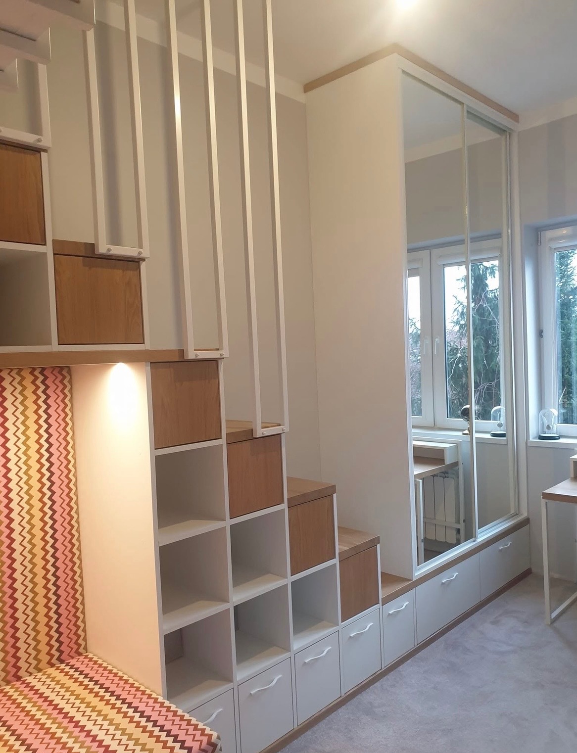 Funkcjonalna zabudowa pokoju: szafa wnękowa z lustrzanymi drzwiami przesuwnymi, schody z szufladami i regałami, tapicerowany zagłówek w geometryczny wzór.