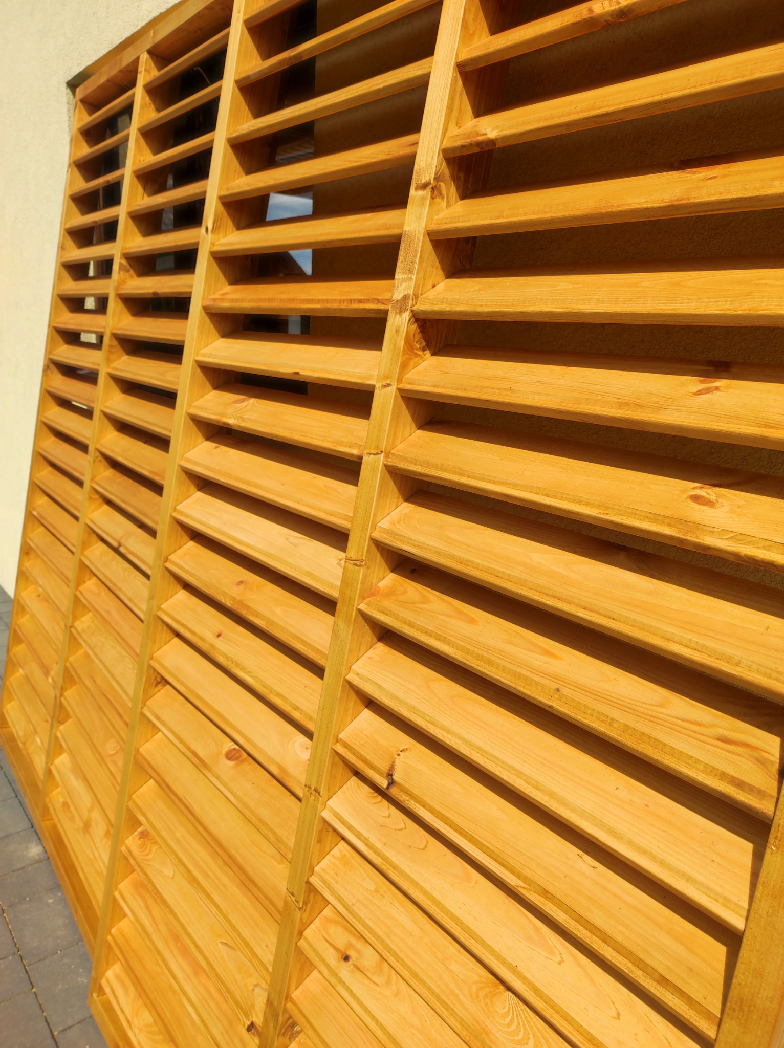 Drewniana konstrukcja z poziomych listew, tworząca osłonę lub element dekoracyjny, świeżo po impregnacji, z widoczną strukturą drewna i delikatnym połyskiem.