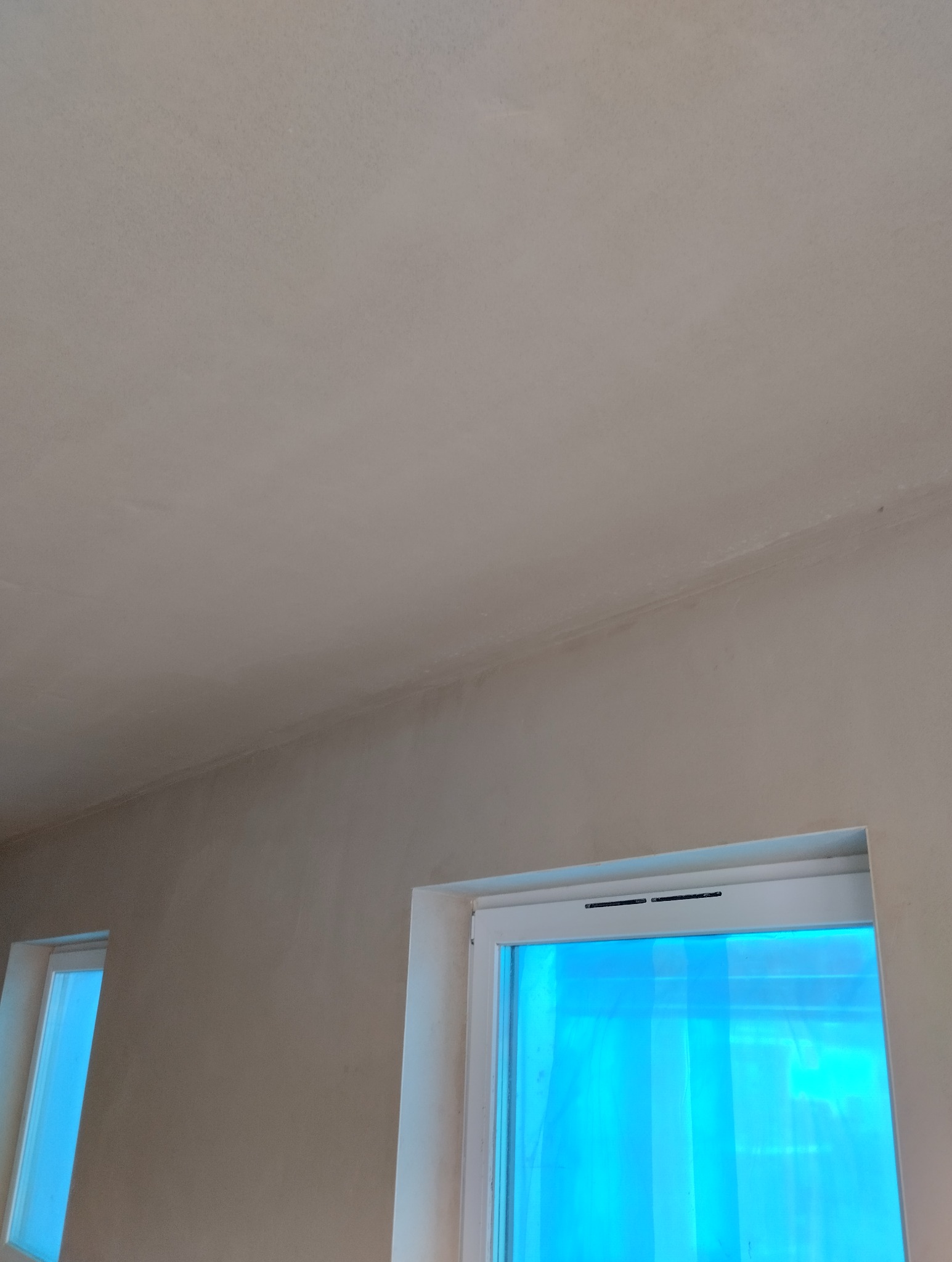 Świeżo nałożona, jasna warstwa na ścianie i suficie, widoczne dwa okna zabezpieczone folią ochronną.