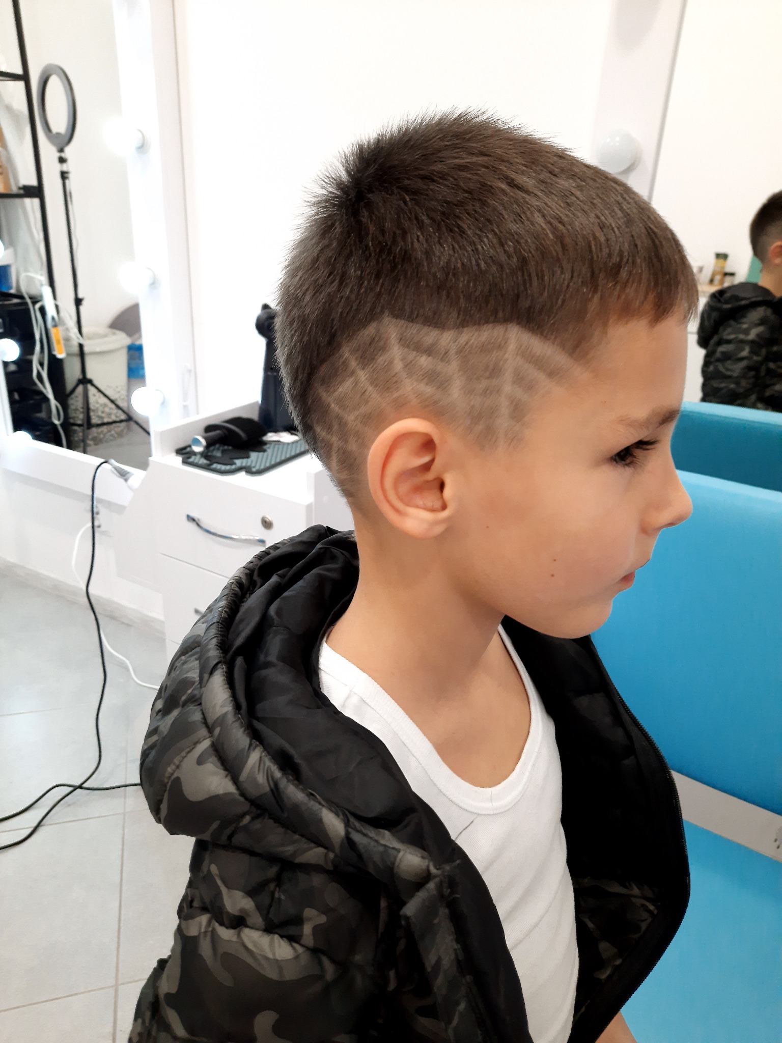 Chłopiec z wyciętym wzorem geometrycznym we włosach, widok z profilu w salonie fryzjerskim.
