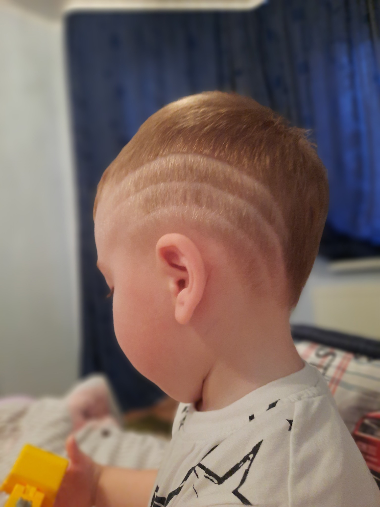 Profil dziecka z wygolonymi liniami na włosach, wzór geometryczny, jasne włosy, biała koszulka.