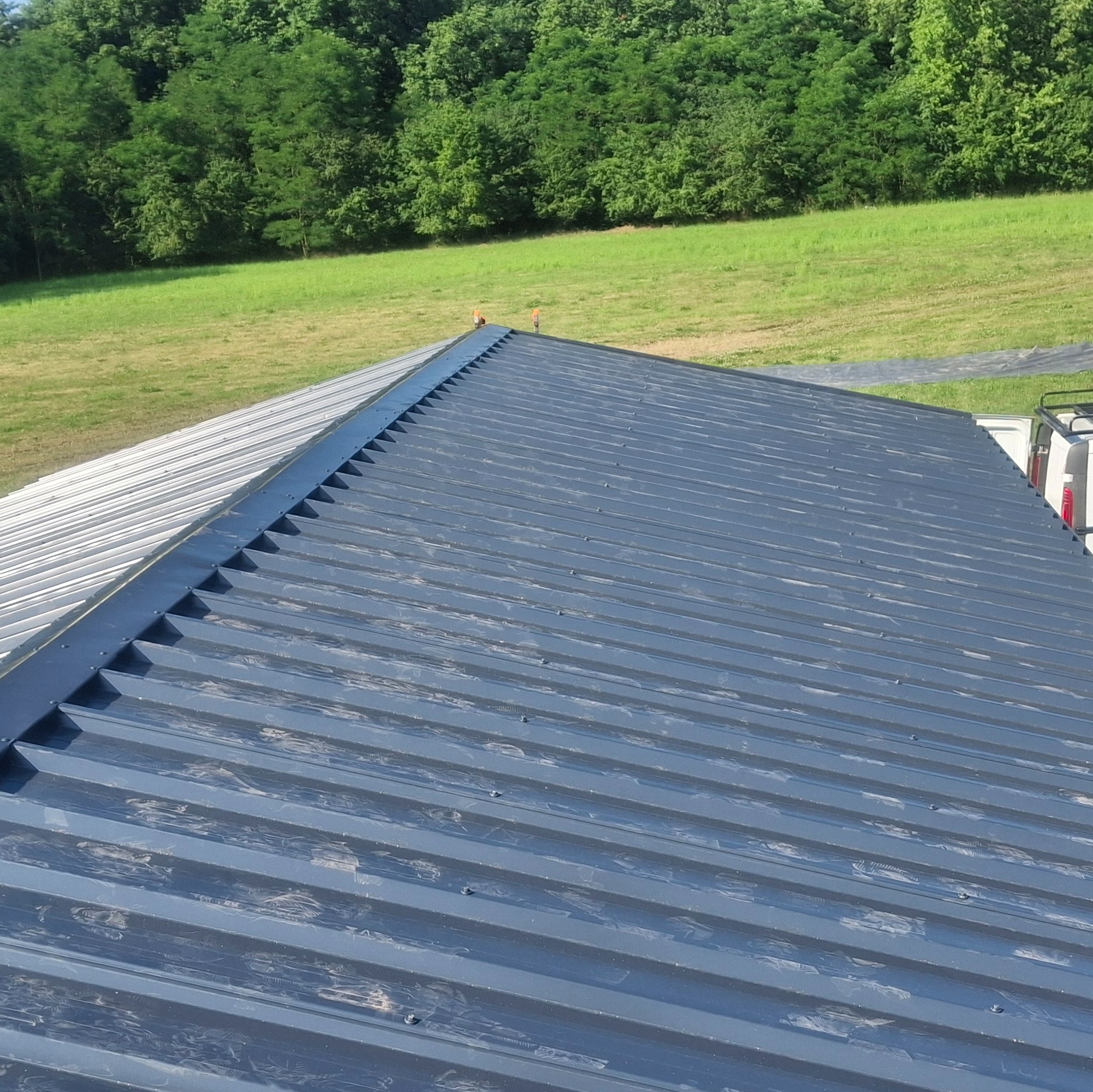 Szary, blaszany dach z widocznymi mocowaniami, na tle zielonego krajobrazu. Ujęcie z góry, ukazujące fakturę blachy i estetykę wykonania.