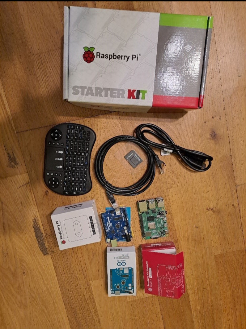 Zestaw startowy Raspberry Pi z miniaturową klawiaturą, przewodami, kartą pamięci i płytkami Arduino na drewnianej podłodze.