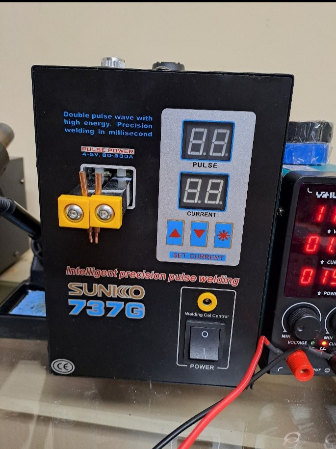 Zbliżenie na spawarkę punktową Sunko 737G z żółtymi elektrodami i wyświetlaczem ustawień prądu i pulsu, widoczne przewody zasilające.