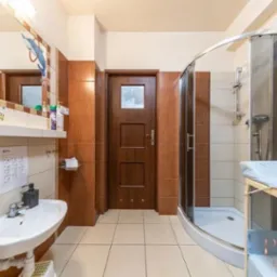 Łazienka w żłobku z umywalką, kabiną prysznicową i przewijakiem, dekorowana naklejkami z motywami morskimi i instrukcjami higieny na ścianie.