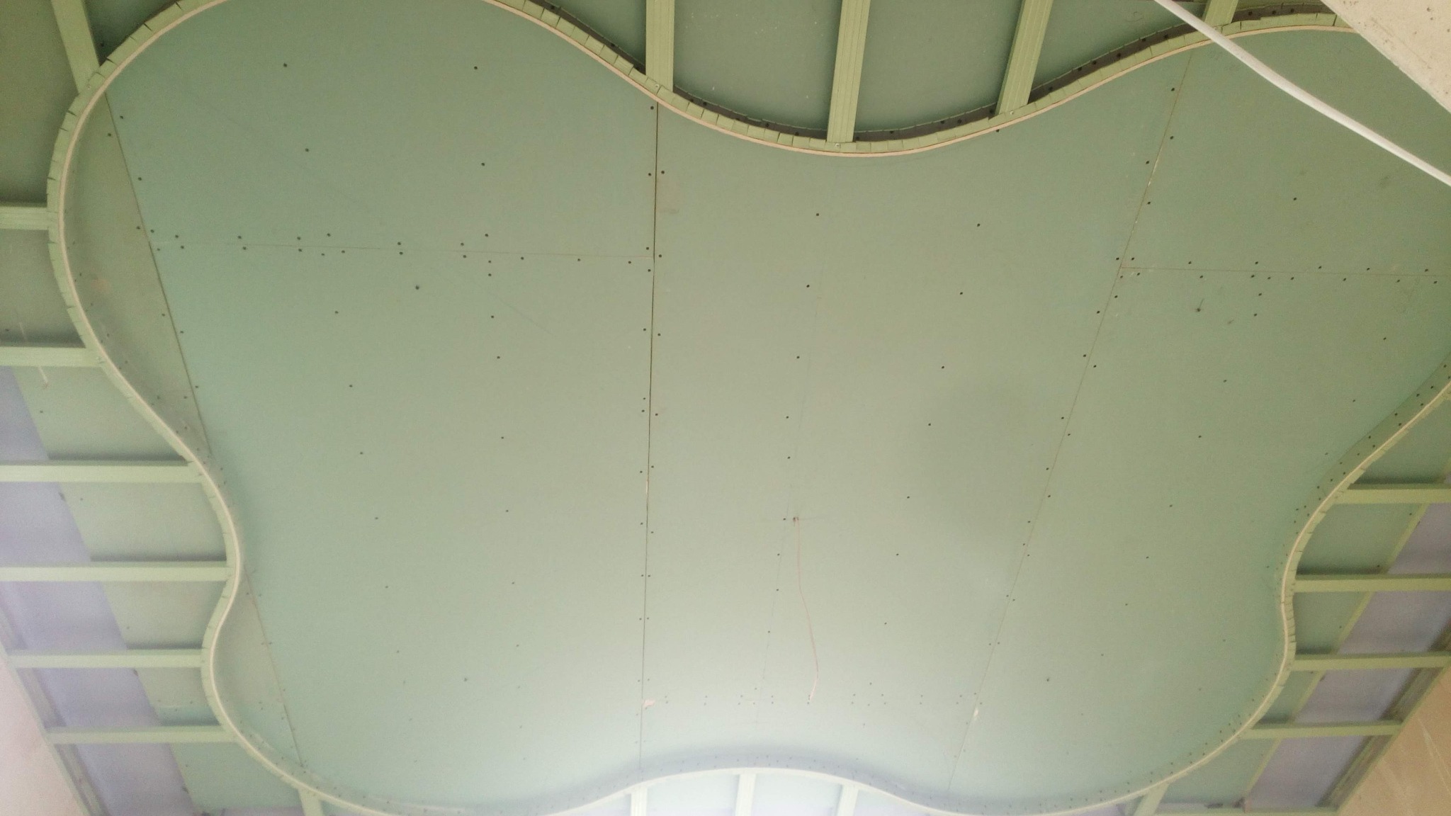 Nietypowy sufit podwieszany z płyt gipsowych o zaokrąglonym, nieregularnym kształcie, widoczne łączenia płyt i elementy konstrukcyjne podtrzymujące sufit.