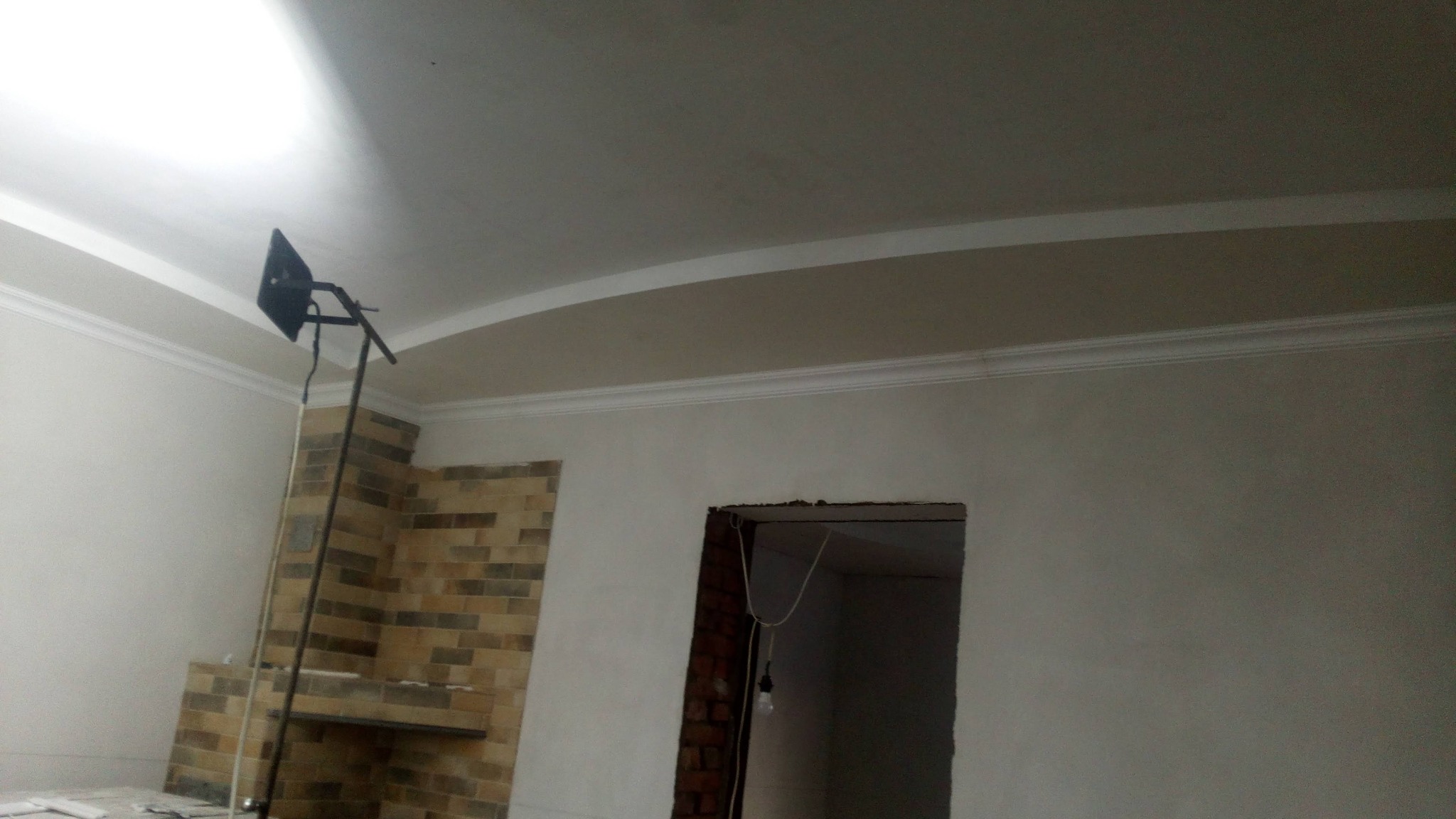 Montaż sufitu z dekoracyjną listwą przysufitową, widoczny halogen na statywie i fragment ściany z cegły