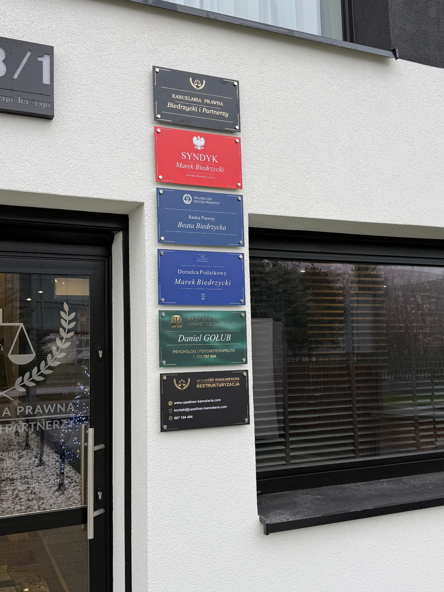 Tabliczki informacyjne z nazwami kancelarii prawnych i doradców, umieszczone na elewacji budynku w Białymstoku. Widoczne logo i dane kontaktowe.