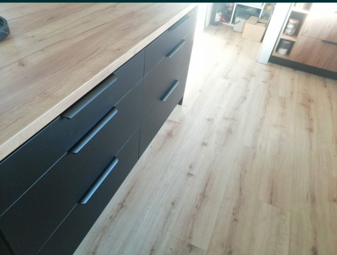 Ciemne szuflady kuchenne z drewnianym blatem i podłogą z paneli w odcieniach beżu i brązu, widok z góry pod kątem.