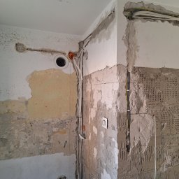 Karol Andrzejewski - Ściana w trakcie remontu z widocznymi przewodami elektrycznymi w bruzdach, przygotowana pod tynkowanie. Fragment ściany z pozostałościami po płytkach.