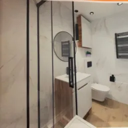 Wizualizacja łazienki z kabiną prysznicową typu walk-in z czarnymi profilami, okrągłym lustrem i grzejnikiem drabinkowym w kolorze czarnym na ścianie z marmurowym wzorem.