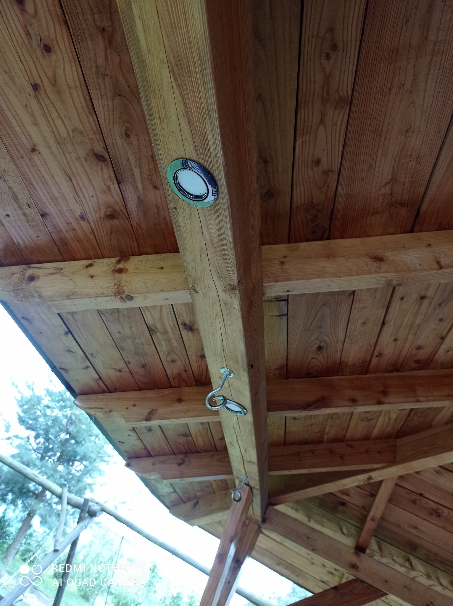 Drewniany sufit altany z zamontowanym oświetleniem punktowym i metalowymi uchwytami na hakach.