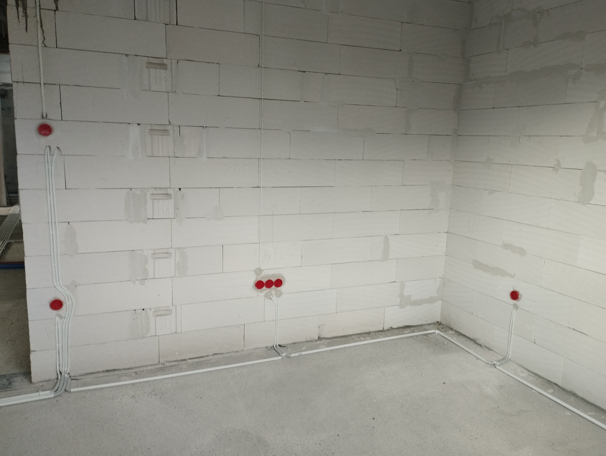 Wewnętrzne okablowanie elektryczne z czerwonymi puszkami instalacyjnymi na ścianie z betonu komórkowego, prowadzone wzdłuż podłogi i pionowo po ścianach.