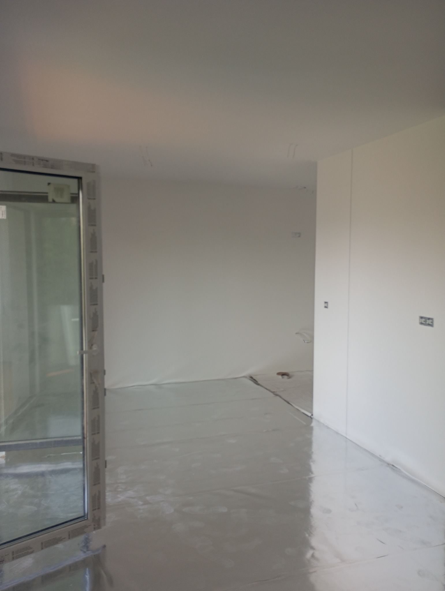 Przygotowane pomieszczenie do prac wykończeniowych: podłoga i ściany zabezpieczone folią malarską, widoczny fragment okna.