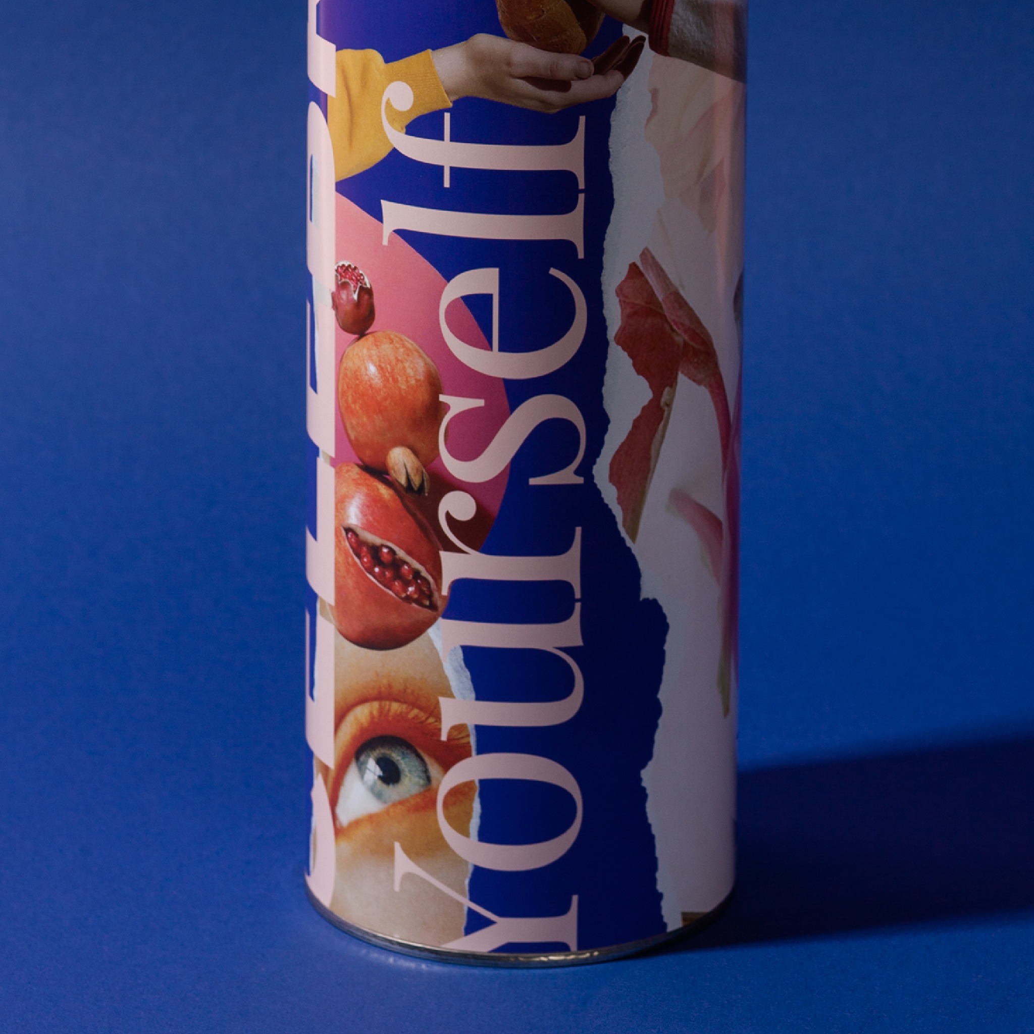 Cylindryczny obiekt z kolażem graficznym, zawierającym elementy takie jak przekrojone granaty, ludzkie oko, dłonie i abstrakcyjne kształty na niebieskim tle.