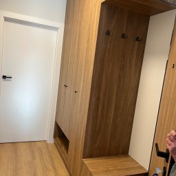 Włodarczyk Meble - Sandra Włodarczyk - Drewniana szafa wnękowa z siedziskiem i wieszakami w przedpokoju, widok z perspektywy podłogi, drzwi wejściowe po lewej stronie, klucze w zamku.