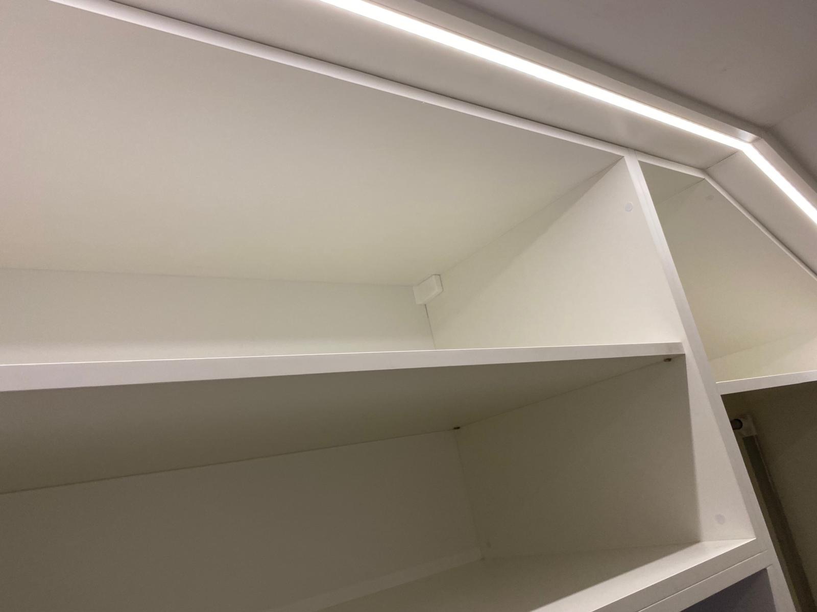 Wnętrze białej szafy z półkami, oświetleniem LED i widocznymi mocowaniami. Ujęcie z dołu, podkreślające przestrzeń i precyzję wykonania.