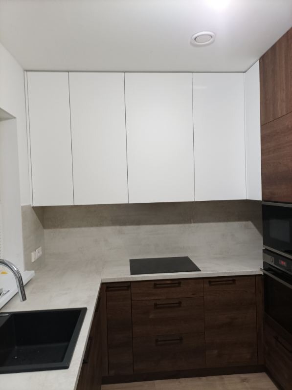 Nowoczesna kuchnia z białymi szafkami górnymi i dolnymi szafkami z ciemnego drewna, z czarnym zlewem i płytą indukcyjną na blacie z szarego kamienia.