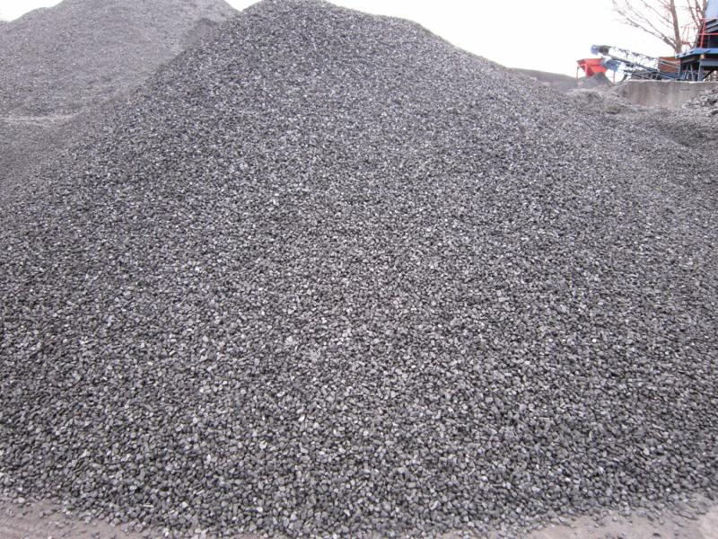 Duży pryzmatyczny stos szarego, drobnego paliwa stałego na tle urządzeń przemysłowych.