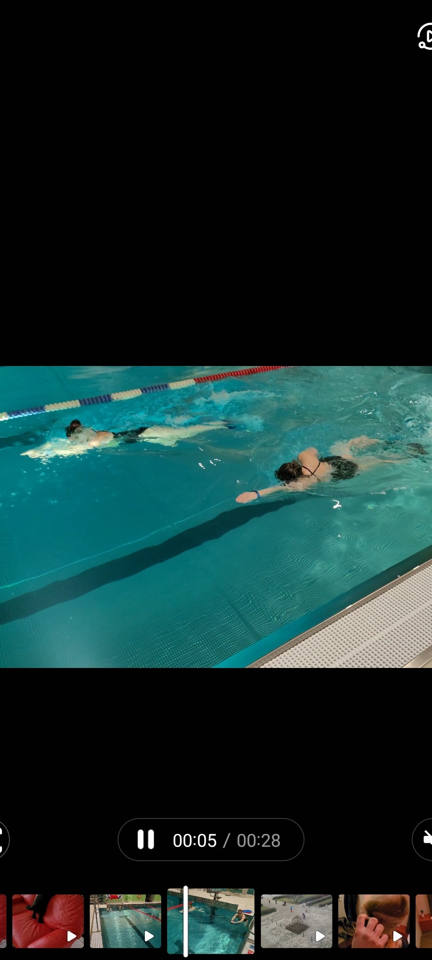 Dwie osoby płynące w basenie krytym, widoczne linie torów i kafelki na brzegu basenu.