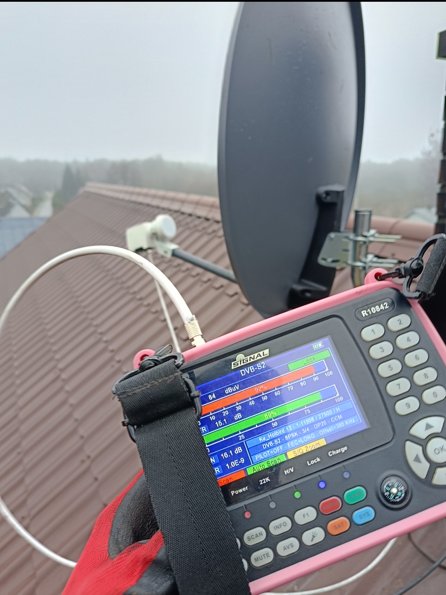 Instalator w rękawicy mierzy sygnał anteny satelitarnej na dachu za pomocą miernika sygnału satelitarnego R10842.