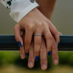 Dłonie pary splecione, pierścionek z kolorowymi oczkami na palcu kobiety, manicure w kolorze głębokiego błękitu.