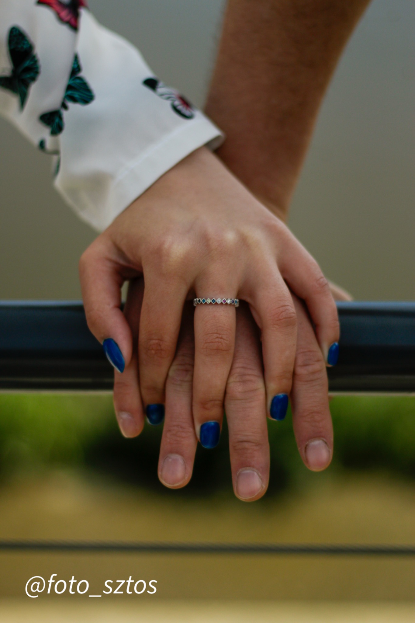 Dłonie pary splecione, pierścionek z kolorowymi oczkami na palcu kobiety, manicure w kolorze głębokiego błękitu.