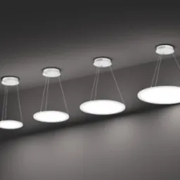 Cztery okrągłe lampy LED wiszące na cienkich linkach, różnej wielkości, ustawione w rzędzie na tle szarego sufitu.