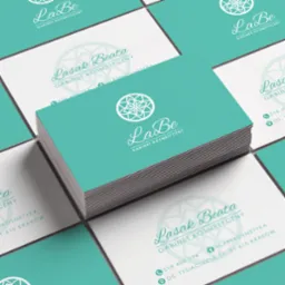 Stos wizytówek w kolorze turkusowym i białym, z logo i danymi kontaktowymi gabinetu kosmetycznego, ułożonych na tle z innymi wizytówkami tej samej firmy.