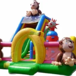 Kolorowy, dmuchany plac zabaw z motywem małp i bananów, zawierający zjeżdżalnię i elementy do wspinaczki.