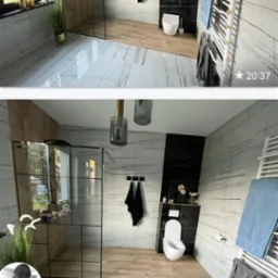 Nowoczesna łazienka z przeszkloną kabiną prysznicową, biało-czarnymi płytkami imitującymi marmur, drewnianą podłogą, podwieszaną toaletą i grzejnikiem drabinkowym z ręcznikami.