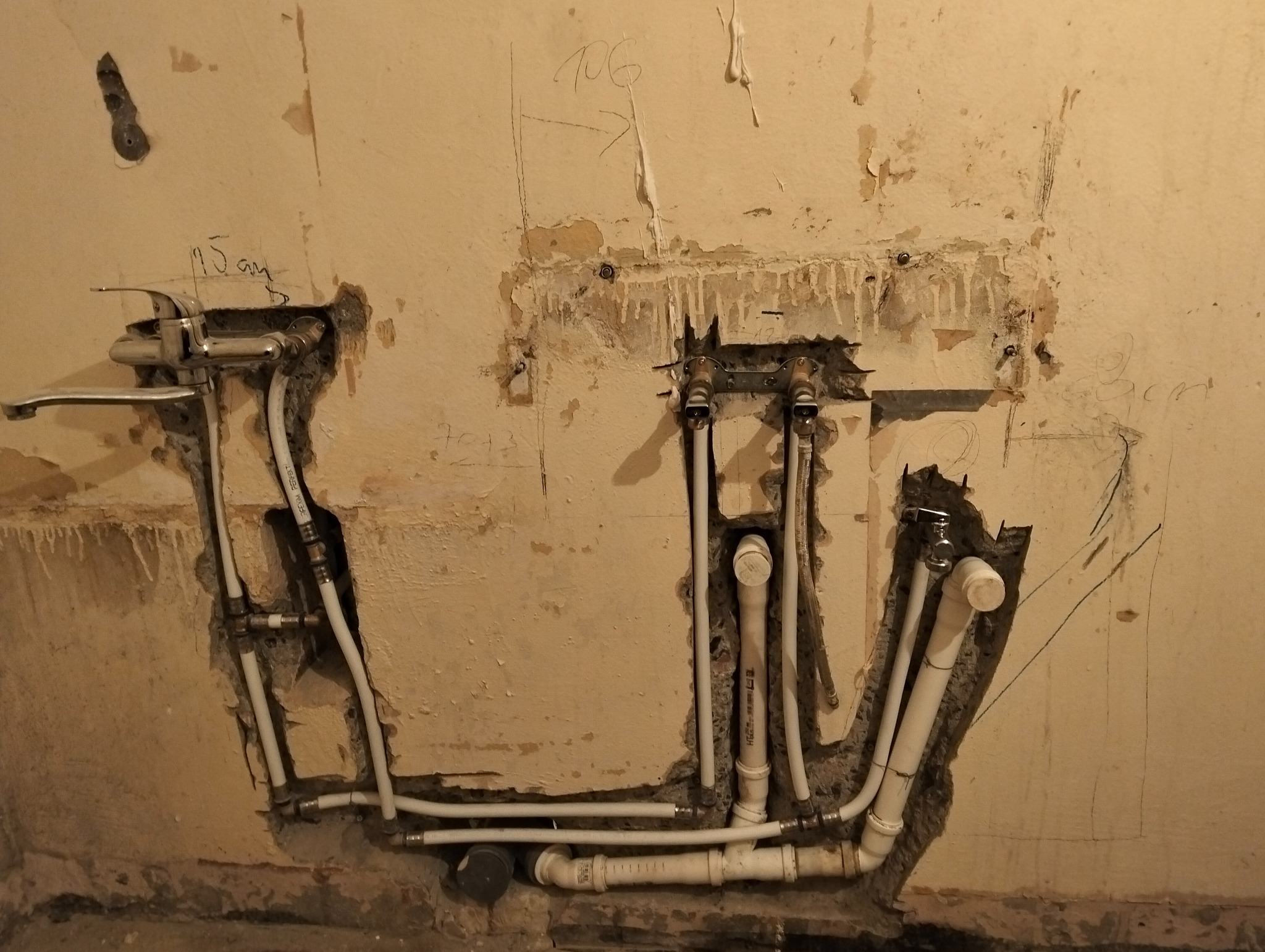 Świeżo zamontowana bateria umywalkowa z podłączeniami rur PEX w surowej ścianie z widocznymi śladami po kuciu i zapiskami ołówkiem.