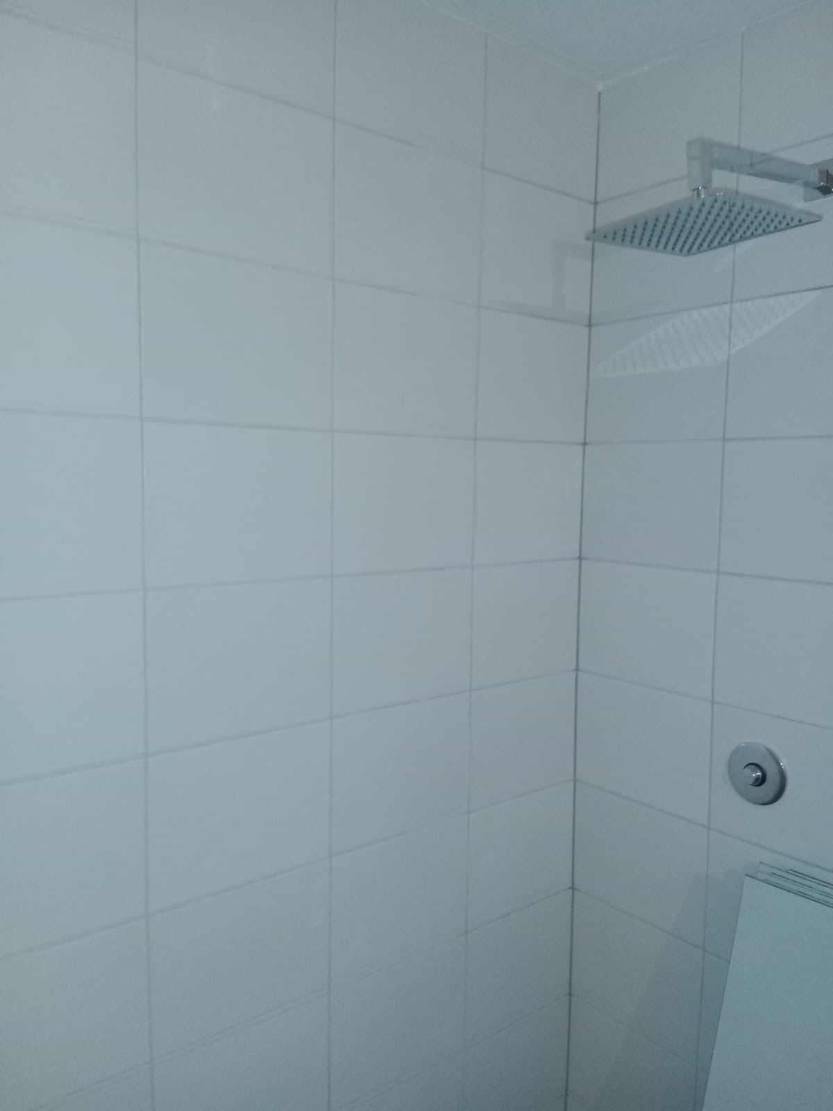 Nowoczesna kabina prysznicowa z kwadratową deszczownicą i minimalistycznym panelem sterowania, wyłożona białymi, kwadratowymi płytkami.