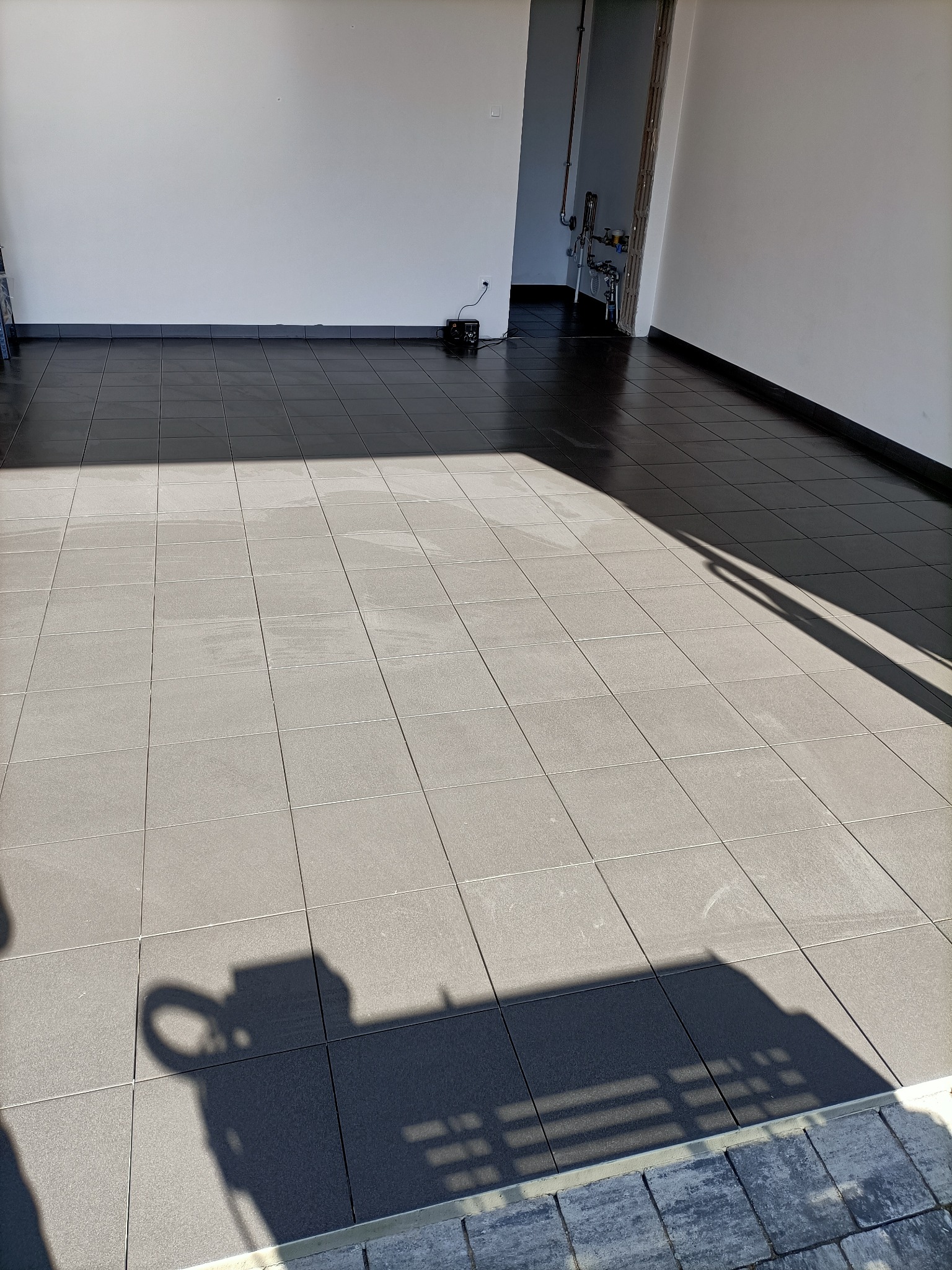 Ułożona podłoga z ciemnych płytek w nowym pomieszczeniu, widoczny cień osoby robiącej zdjęcie