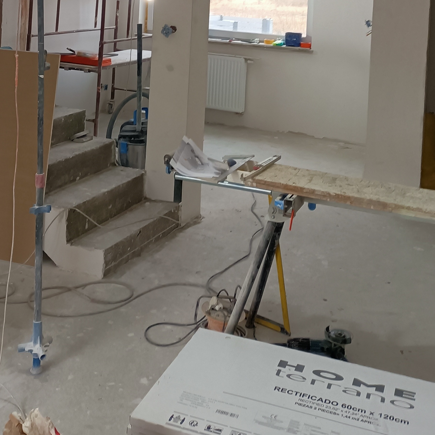Wnętrze w trakcie remontu w Kaliszu: widoczne schody w surowym stanie, narzędzia, płyty gipsowe i stojak roboczy, sygnalizujące prace wykończeniowe.