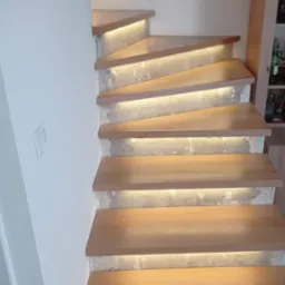 Drewniane schody z podświetleniem LED, zamontowane na surowym betonie, widok z dołu, oświetlenie ciepłe.