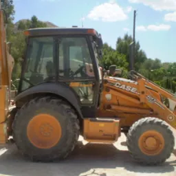 Pomarańczowa koparko-ładowarka CASE 580 Super R Series 2, zaparkowana na placu z widocznym drzewem w tle.