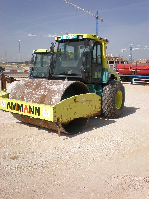 Dwa walce drogowe marki Ammann na placu budowy, w tle dźwigi budowlane i budynki w trakcie wznoszenia.