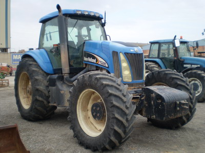 Niebieski traktor New Holland TD5050 z dużymi oponami, widoczny z przodu na żwirowym podłożu, z drugim traktorem w tle.