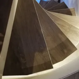 Spiralne schody wykończone panelami podłogowymi w odcieniach brązu i beżu, widok z góry.