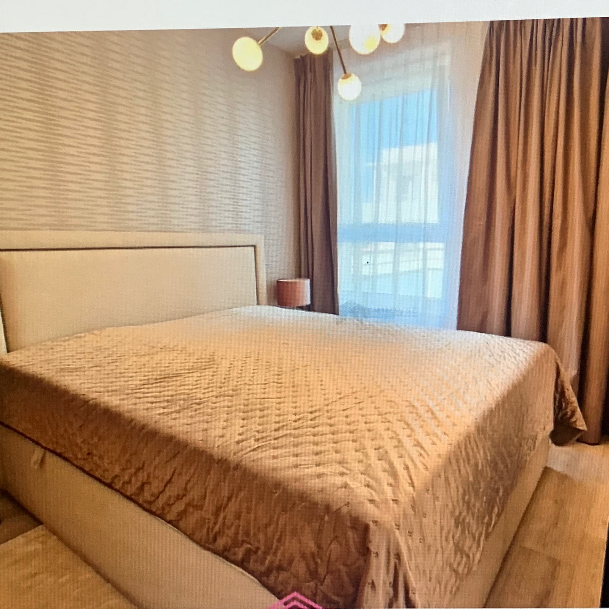 Beżowa sypialnia z dużym łóżkiem, wzorzystą tapetą i nowoczesną lampą sufitową z kulistymi kloszami.