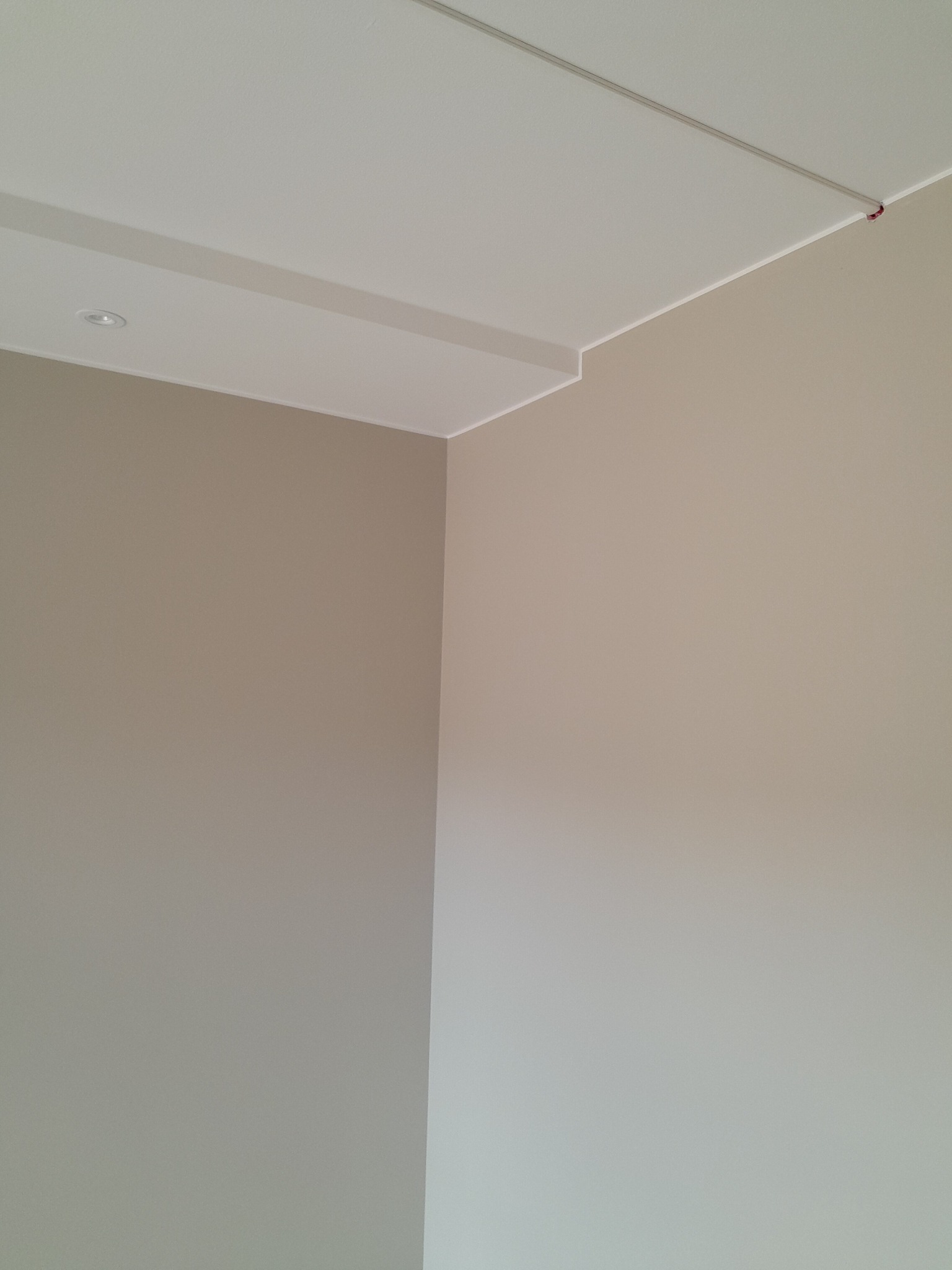 Pomieszczenie po malowaniu ścian w odcieniach beżu, z widocznym wykończeniem sufitu, listwa przypodłogowa i wbudowane oświetlenie sufitowe.