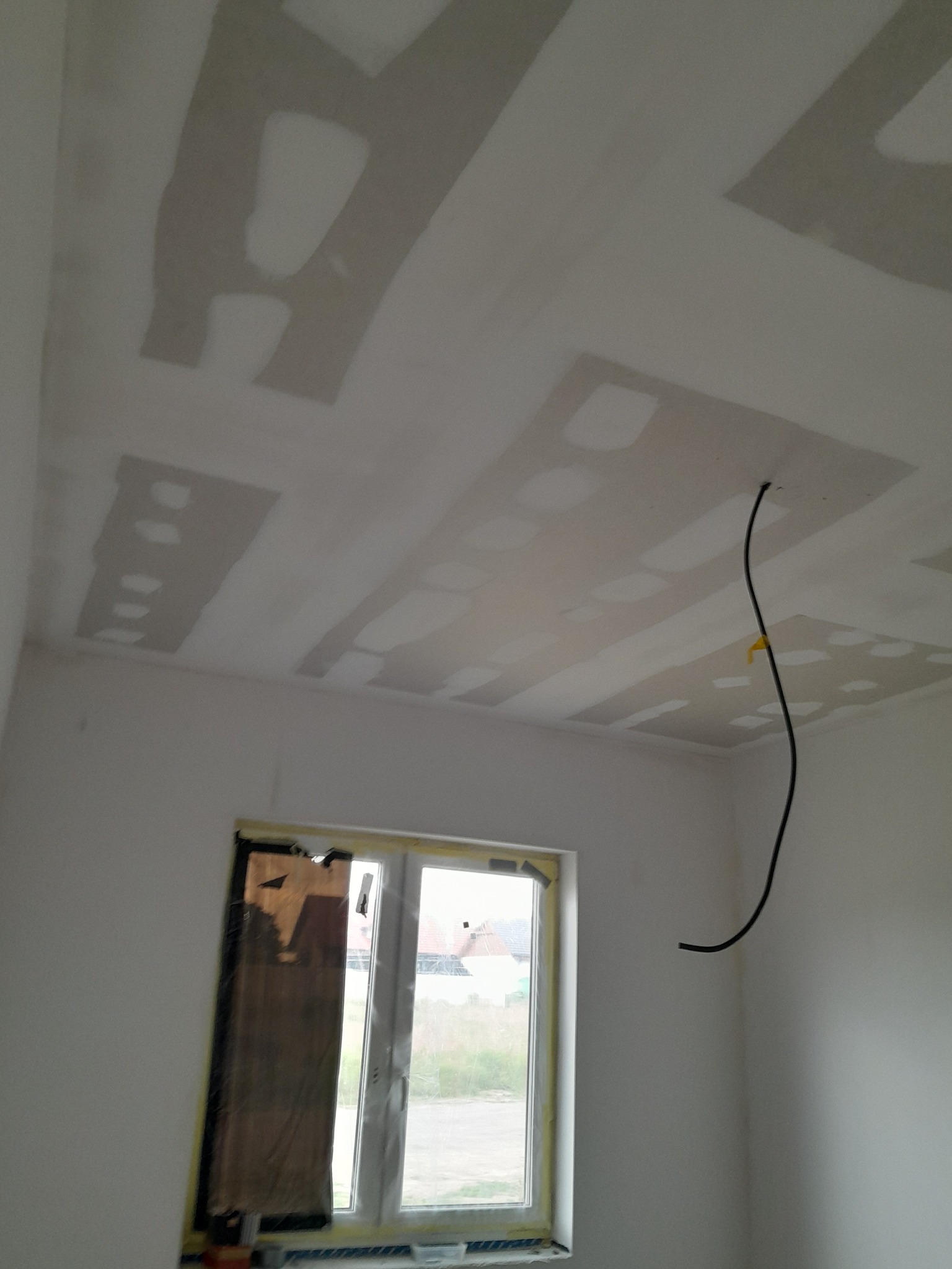 Przygotowanie sufitu do malowania: widoczne płyty gipsowo-kartonowe ze szpachlowanymi łączeniami, zabezpieczone okno, wystający kabel elektryczny.