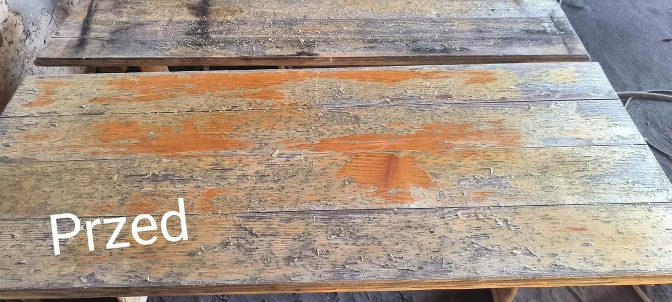 Dwa drewniane blaty stołów w stanie surowym, z resztkami starej farby i wyraźnymi śladami korozji, przygotowane do odnowienia.